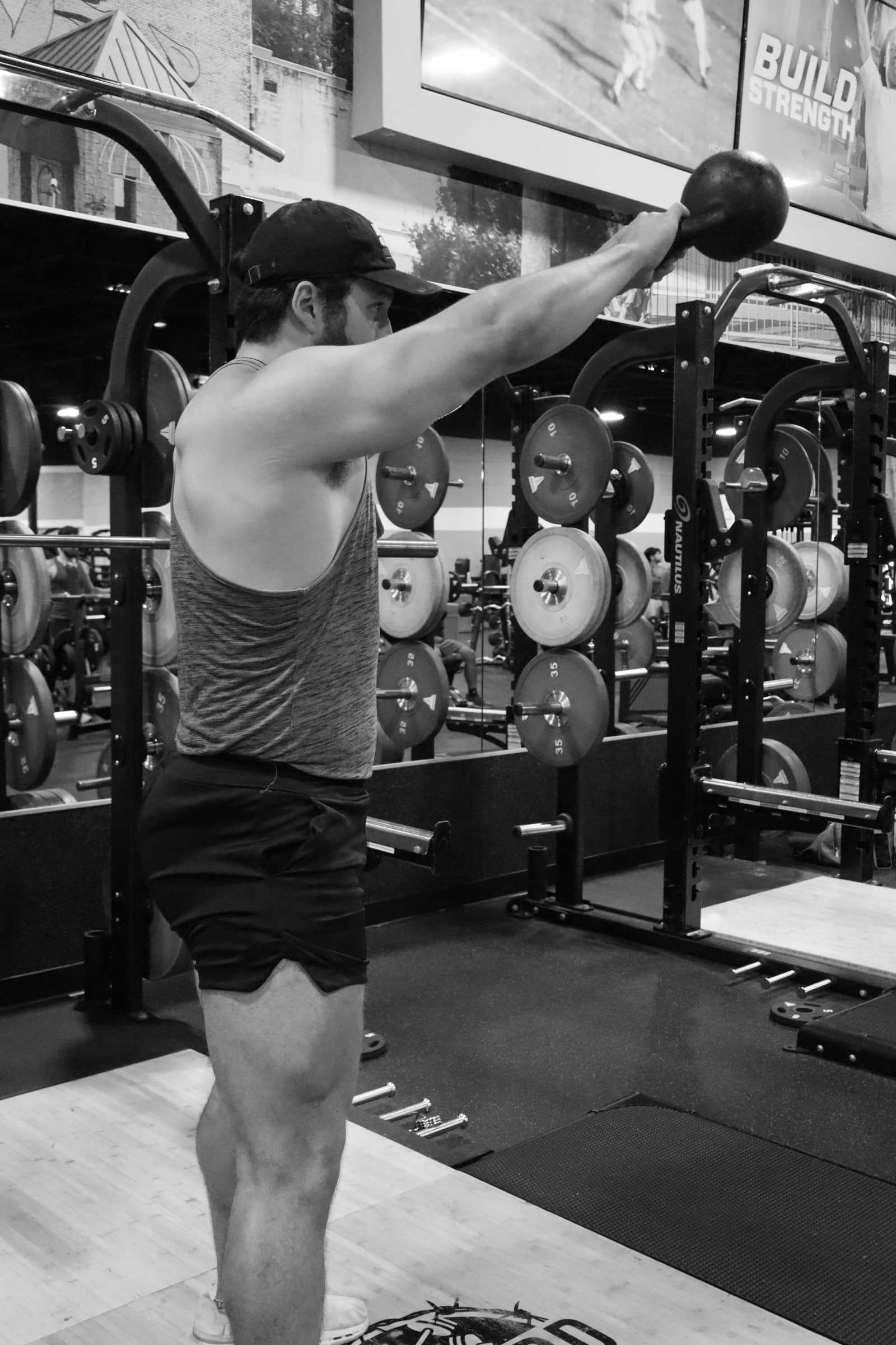 A lifter at the top of a kettlebell swing in front of a squat rack